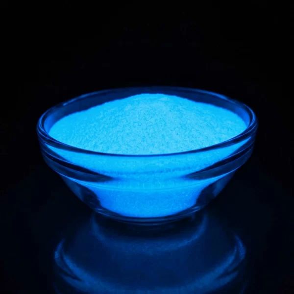 Glowing blue powder in a clear glass bowl against a dark background